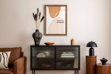 Interior design of stylish living room with mock up poster frame, black commode, stylish brown sofa, wooden stand, lamp, vase with dried flowers and personal accessories. Home decor. Template. 