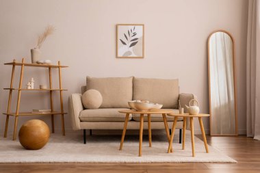 Creative composition of living room interior with mock up poster frame, classic beige sofa, wooden round coffee table, mirror, elegant bowl and stylish personal accessories. Beige wall. Home decor. Template.