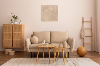 Interior design of cozy living room interior with mock up poster frame, beige sofa, round coffee table, vase with dried flowers, rug, rattan commode and personal accessories. Home decor. Template.