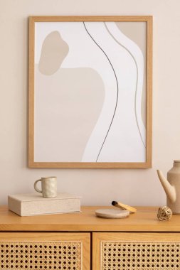 Creative composition of living room interior with mock up poster frame, rattan commode, beige wall, gray cup, box and personal accessories. Home decor. Template. 