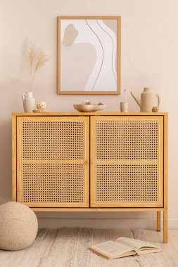 Sunny living room interior with mock up poster frame, stylish rattan commode, round pillow, vase with dried flowers, book and personal accessories. Home decor. Template. 