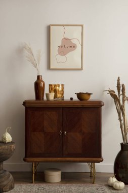 Creative composition of vintage living room interior with mock up poster frame, stylish sideboard, round wooden stand, vase with dried flowers, patterned carpet and personal accessories. Home decor. Template. 
