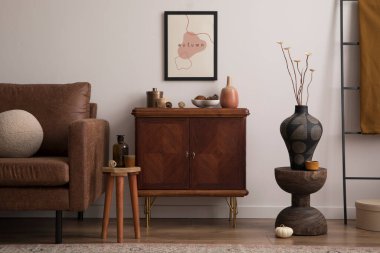 Interior design of cozy living room interior with mock up poster frame, brown sofa, sideboard, glass bottle, bowl with coconut, plaid, round pillows and personal accessories. Home decor. Template.