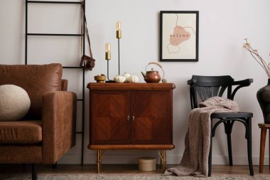 Warm and cozy living room interior with mock up poster frame with vintage sideboard, stylish black chair, box, patterned carpet, pumpkins, brown sofa and personal accessories. Home decor. Template. 
