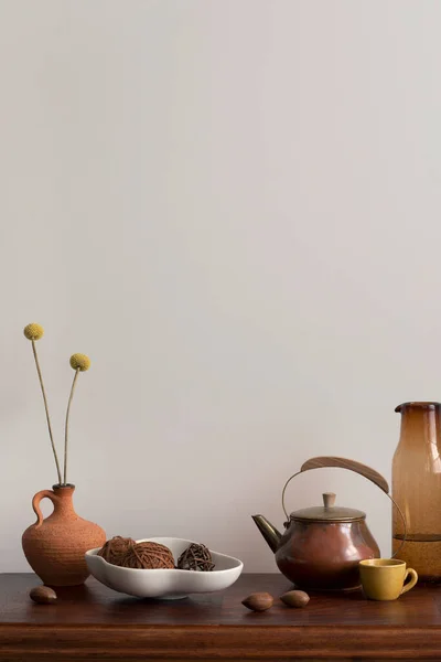 Minimalist composition of living room interior with orange vase with dried flowers, stylish bowl with ball, nuts, brown pitcher, glass carafe and personal accessories. Home decor. Template.