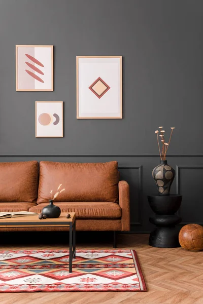 Aesthetic interior of living room with mock up poster frame, brown sofa, wooden coffee table, black lamp, patterned rug, gray wall, plants in flowerpot and personal accessories. Home decor. Template.