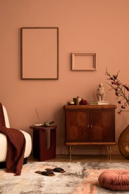 Cozy living room interior with mock up poster frame, wooden sideboard, glass vase with rowan, books, rug, sculpture, gold casket, and personal accessories. Home decor. Template.