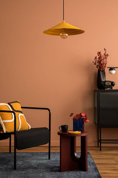 Warm and cozy living room interior with black armchair, round coffee table, patterned pillow, glass commode, navy carpet, vase with dried flowers and personal accessories. Home decor. Template.
