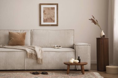 Interior design of elegant living room with mock up poster frame, modern beige sofa, brown pillow, wooden stand, vase with dried flowers, carpet, books and personal accessories. Home decor. Template. 