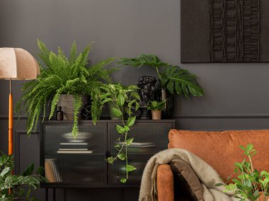 Aesthetic interior of living room with mock up poster frame, brown sofa, glass sideboard, plants in flowerpots, lamp, beige plaid, pillow, sculpture and personal accessories. Home decor. Template.