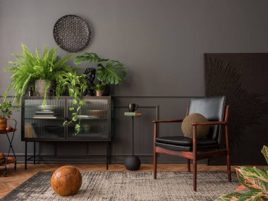 Interior design of elegant living room interior with mock up poster frame, leather armchair, glass sideboard, plants, pillows, rug, black wall, books and personal accessories. Home decor. Template. 