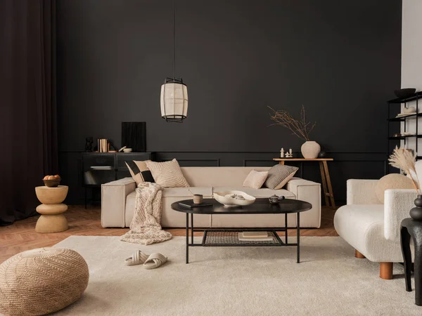 Creative composition of living room interior with modular beige sofa, black coffee table, armchair, rug, black wall with stucco, vase with dried flowers and personal accessories. Home decor. Template.