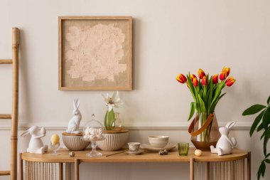 Interior design of easter living room interior with mock up poster frame, glass vase with tulips, wooden sideboard, easter bunny sculpture, bowl, ladder, and personal accessories. Home decor. Template
