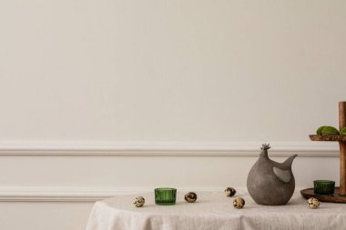 Minimal spring composition of easter living room interior with copy space, beige wall with stucco hen sculpture, green glass, quail eggs and personal accessories. Home decor. Template. 