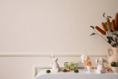 Creative composition of easter living room interior with copy space, beige vase with dried flowers, glass eggs, easter bunny sculpture and personal accessories. Home decor. Template.