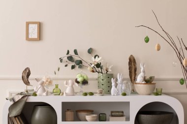 Interior design of easter living room interior stylish sideboard, colorful easter eggs, easter bunny sculpture, vase with leaves, magnolia and personal accessories Home decor. Template.
