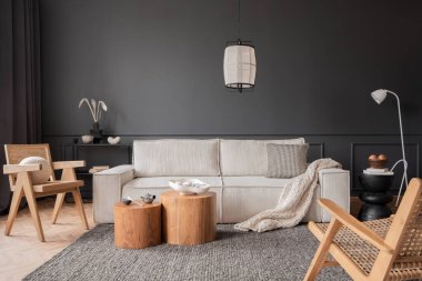 Interior design of living room interior with modular sofa, wooden coffee table, dark wall, rattan armchair, grey rug, beige bowl, patterned pillow, lamp and personal accessories. Home decor. Template.