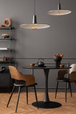 Minimalist composition of living room interior with black round coffee table, stylish chair, wooden sideboard, dark wall with stucco, pitcher, lamp and personal accessories. Home decor. Template.