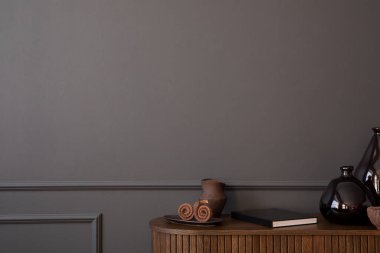 Minimalist composition of living room interior with copy space, dark wall with stucco, wooden sideboard, glass vase, book, bowl and personal accessories. Home decor. Template. 