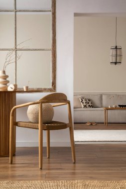 Minimalist composition of open space interior with wooden chair, round pillow, vase with dried flowers, modular sofa, patterned pillow, window, beige rug and personal accessories. Home decor. Template