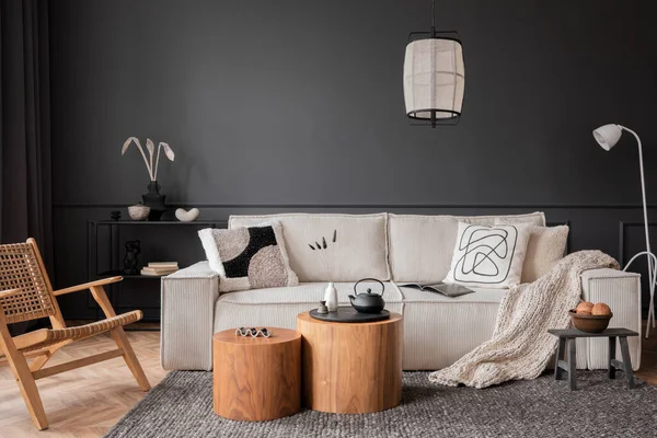 Interior design of living room interior with modular sofa, wooden coffee table, dark wall, rattan armchair, grey rug, beige bowl, patterned pillow, lamp and personal accessories. Home decor. Template.
