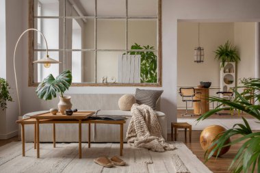 Open space interior with modular sofa, wooden coffee table, big window, beige rug, braided plaid, pillows, round table, lamp, plants, slippers, ball and personal accessories. Home decor. Template.