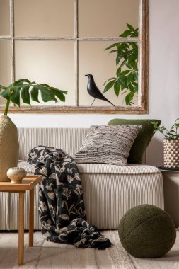 Warm and cozy living room interior with beige modular sofa, big window, patterned pillows, braided plaid, black bird, vase with leaves, plants,  and personal accessories. Home decor. Template. 