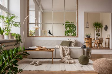 Open space interior with modular sofa, wooden coffee table, big window, patterned pillows, braided plaid, stylish lamp, wooden coffee table, plants and personal accessories. Home decor. Template.