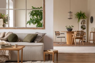 Interior design of cozy open space with modular sofa, green pillows, braided plaid, wooden coffee table, rattan armchair, round table, plants and personal accessories. Home decor. Template. 