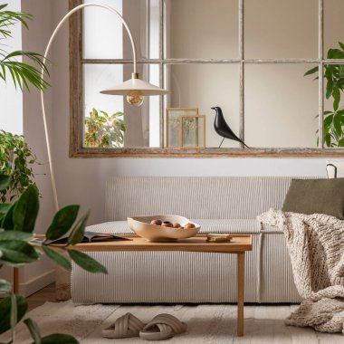 Open space interior with modular sofa, wooden coffee table, big window, patterned pillows, braided plaid, stylish lamp, wooden coffee table, plants and personal accessories. Home decor. Template.