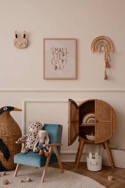 Çocuk odasının iç kısmının minimalist kompozisyonu. Poster çerçevesi mavi koltuk, pelüş oyuncaklar, tahta bloklar, ahşap büfe, bej duvar, sıva, örülmüş penguen ve kişisel aksesuarlar. Ev dekoru. Şablon.