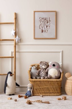 Çocuk odasının içinde poster çerçevesi, hasır sepet, peluş hayvan oyuncakları, tahta bloklayıcılar, beyaz tabure, sıva ve kişisel aksesuarlarla bej duvar. Ev dekoru. Şablon.