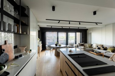 Mutfak odasının modern kompozisyonu mutfak adası, siyah fahişeler, siyah indüksiyon hob, gri masa, çiçekler, mobilyalar, büyük pencere ve zarif kişisel aksesuarlar. Şık bir ev dekoru. Şablon. 