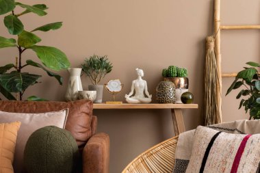 Sıcak ve rahat bir oturma odası içinde renkli yastıklar, ahşap bank, kahverengi kanepe, saksıda çiçekler, örgülü koltuk, şık bir heykel, kahverengi duvar ve kişisel aksesuarlar var. Ev dekoru. Şablon