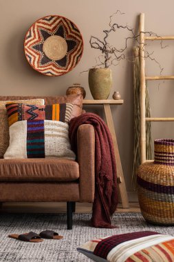 Kahverengi kanepe, renkli yastıklar, desenli sepetler, merdiven terlikleri, dallı vazo ve kişisel aksesuarlarla oturma odasının yaratıcı kompozisyonu. Ev dekoru. Şablon. 