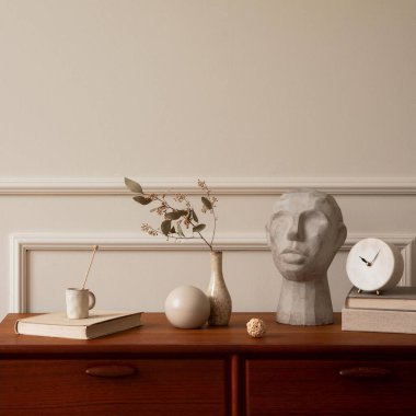 Oturma odasının minimalist kompozisyonu fotokopi alanı, ahşap büfe, kurutulmuş çiçekli vazo, gri heykel, kitaplar, sıva ve kişisel aksesuarlı duvar. Ev dekoru. Şablon.