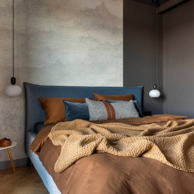 Modern yatak odasının iç kısmının şık bir kompozisyonu. Yatak, yaratıcı lamba ve zarif kişisel aksesuarlar. Beton duvar. Kahverengi çarşaflar. Minimalist erkeksi kavram. Şablon.