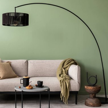 Oturma odasındaki yeşil duvarlı şık kompozisyon, tasarım gri kanepe, sehpa, koyu lamba ve zarif kişisel aksesuarlar. Bej yastık ve ekose kumaş. Samimi bir daire. Şablon.