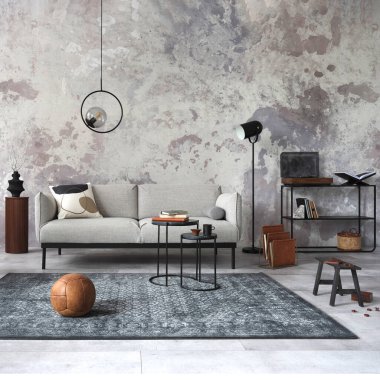 Tasarım gri kanepe, sandalye, yuvarlak lamba, siyah sehpa, dekorasyon, yastık ve zarif aksesuarlarla oturma odasının zarif ve modern kompozisyonu. Beton grunge duvar. 