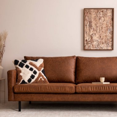 Oturma odasının içi sıcacık, poster şöhreti, kahverengi kanepe, bej halı, desenli yastık, modern pouf, kurumuş çiçekli vazo, dekorasyon ve kişisel aksesuarlarla dolu. Sıcak ev dekorasyonu. Şablon.