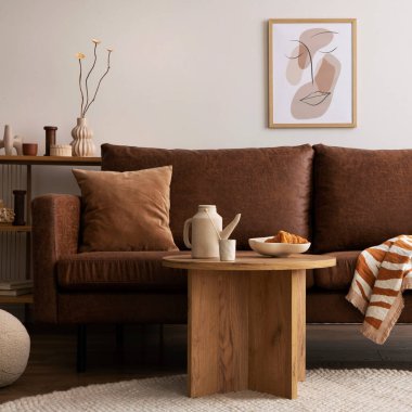 Warm and cozy interior of living room space with brown sofa, round beige carpet, wooden coffee table, mock up poster frames, decoration and elegant personal accessories. Cozy home decor. Template.