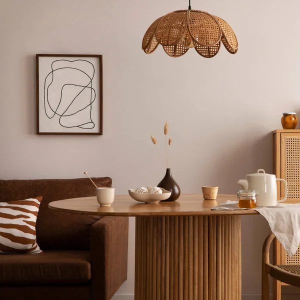 Boho and cozy interior of dining room with round wooden table, design chair, brown sofa, shelf, mock up poster frame, pendant lamp, tea pot, decoration and elegant accessories. Stylish home decor. 