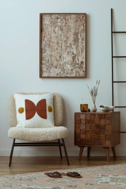 Warm and cozy composition of living room interior with mock up painting frame, boucle armchair, patterned pillow, wooden coffee table, black ladder, vintage carpet, slippers and personal accessories. Home decor. Template.