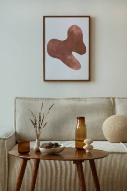 Creative composition of living room interior with mock up poster frame, modern beige sofa, oval wooden coffee table,  round pillow, glass case, craetive bowl with dried fruit, sculpture and personal accessories. Home decor. Template.