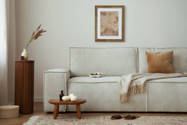 Poster çerçevesi, modern bej kanepe, kahverengi yastık, ahşap tezgah, kurumuş çiçekler, halı, kitaplar ve kişisel aksesuarları olan zarif oturma odasının iç tasarımı. Ev dekoru. Şablon.