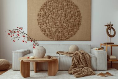 Interior design of living room interior with mock up poster, beige sofa, modern armchair, braided plaid, books, rowan in vase, pouf, lamp, bowl, rug and personal accessories. Home decor. Template.