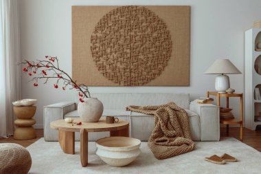 Interior design of living room interior with mock up poster, beige sofa, modern armchair, braided plaid, books, rowan in vase, pouf, lamp, bowl, rug and personal accessories. Home decor. Template.
