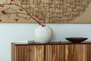 Minimalist composition of living room interior with mock up poster frame, wooden sideboard beige vase with rowan, black bowl, white wall, books and personal accessories. Home decor. Template.