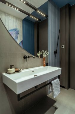 Interior design of bathroom interior with big mirror, white silk, towel, gray tiles, modern lamp, vase with dried flowers and personal accessories. Home decor. Template.