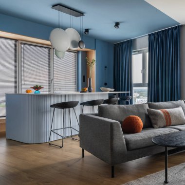 Creative composition of kitchen and living room interior with gray sofa, marble kitchen island, black coffee table, curtain, modern sculpture, gray rug and personal accessories. Home decor. Template.